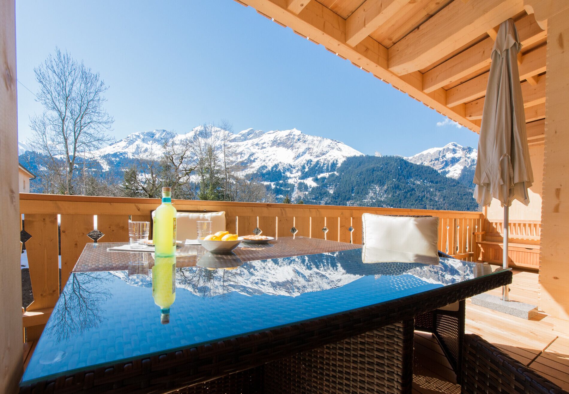 A wooden deck with a glass table, a bottle, and a bowl of fruit.