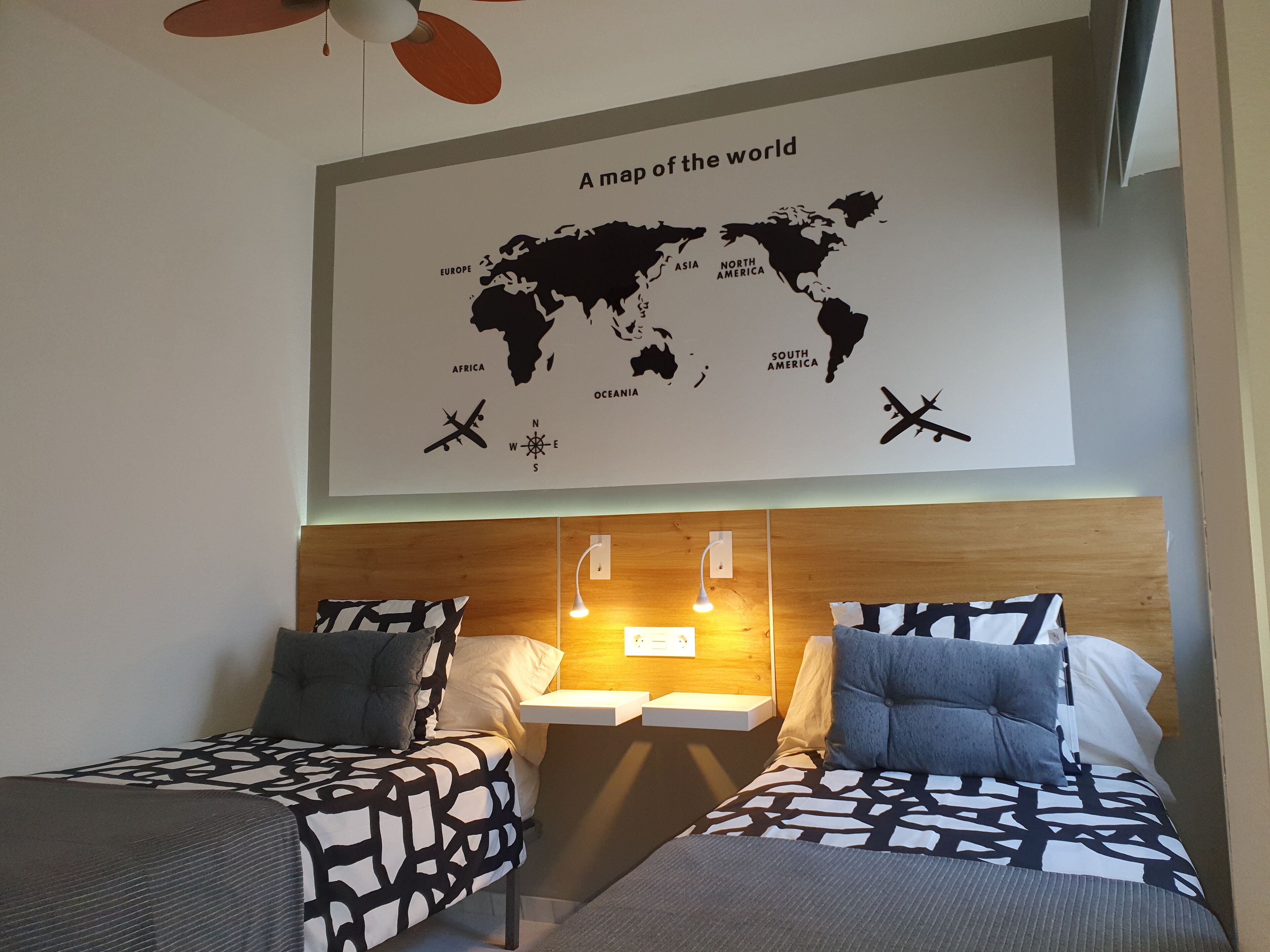 A hotel room with two beds, a world map on the wall, and a ceiling fan.
