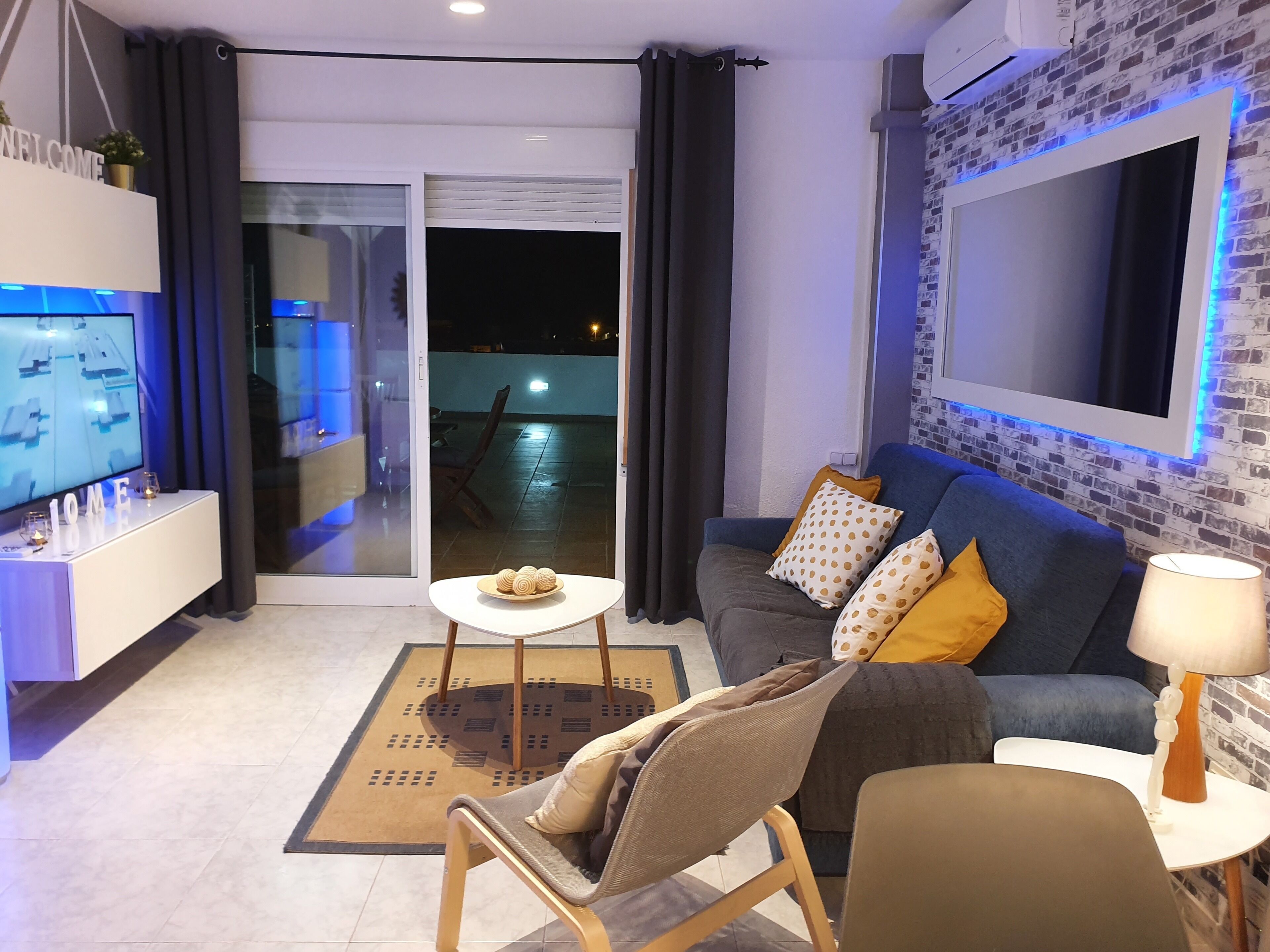 A modern living room with a sofa, a coffee table, and a TV. There is a sliding glass door leading to an outdoor area.