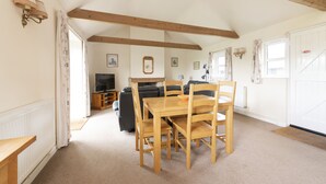 A cozy living room with a wooden dining table and chairs, a sofa, and a television. - Buckingham Cottage : Idyllic Getaway Cottage in the rolling hills of Dorset (West Milton)