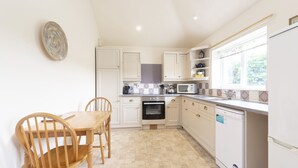 A kitchen with white cabinets, a dining table with chairs, a built-in oven, a microwave, and a dishwasher. - Buckingham Cottage : Idyllic Getaway Cottage in the rolling hills of Dorset (West Milton)