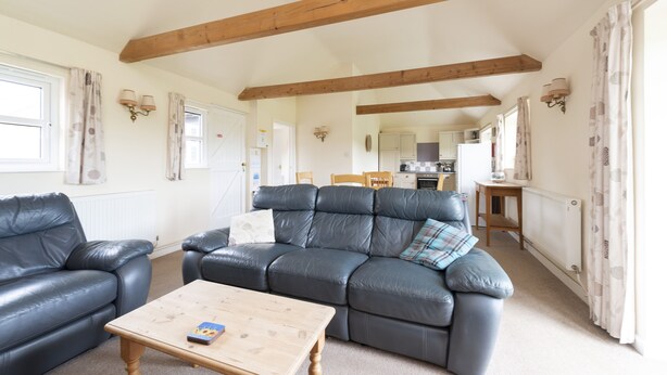 A cozy living room with a leather sofa, a wooden coffee table, and a kitchen in the background. - Buckingham Cottage : Idyllic Getaway Cottage in the rolling hills of Dorset (West Milton)