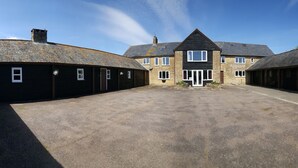 A large stone building with multiple doors and windows, a central entrance, and a gravel driveway. - Buckingham Cottage : Idyllic Getaway Cottage in the rolling hills of Dorset (West Milton)
