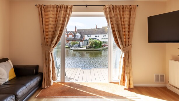 A living room with a black leather sofa, a brown rug, and a view of a canal with houses in the background.