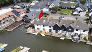 A riverside building with a dock, surrounded by residential houses and parked cars.