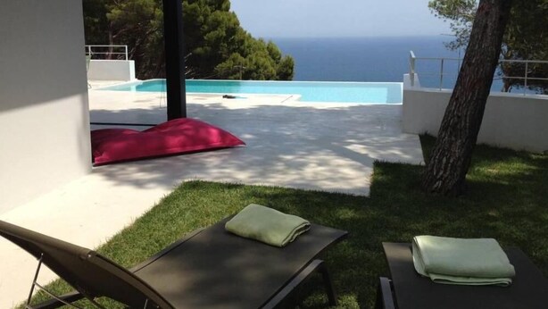 Un espacio exterior moderno con piscina, sillones de descanso y vistas al mar.
