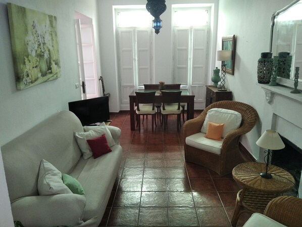 Una sala de estar con sofá, una silla, televisión, mesa de comedor con sillas y chimenea.