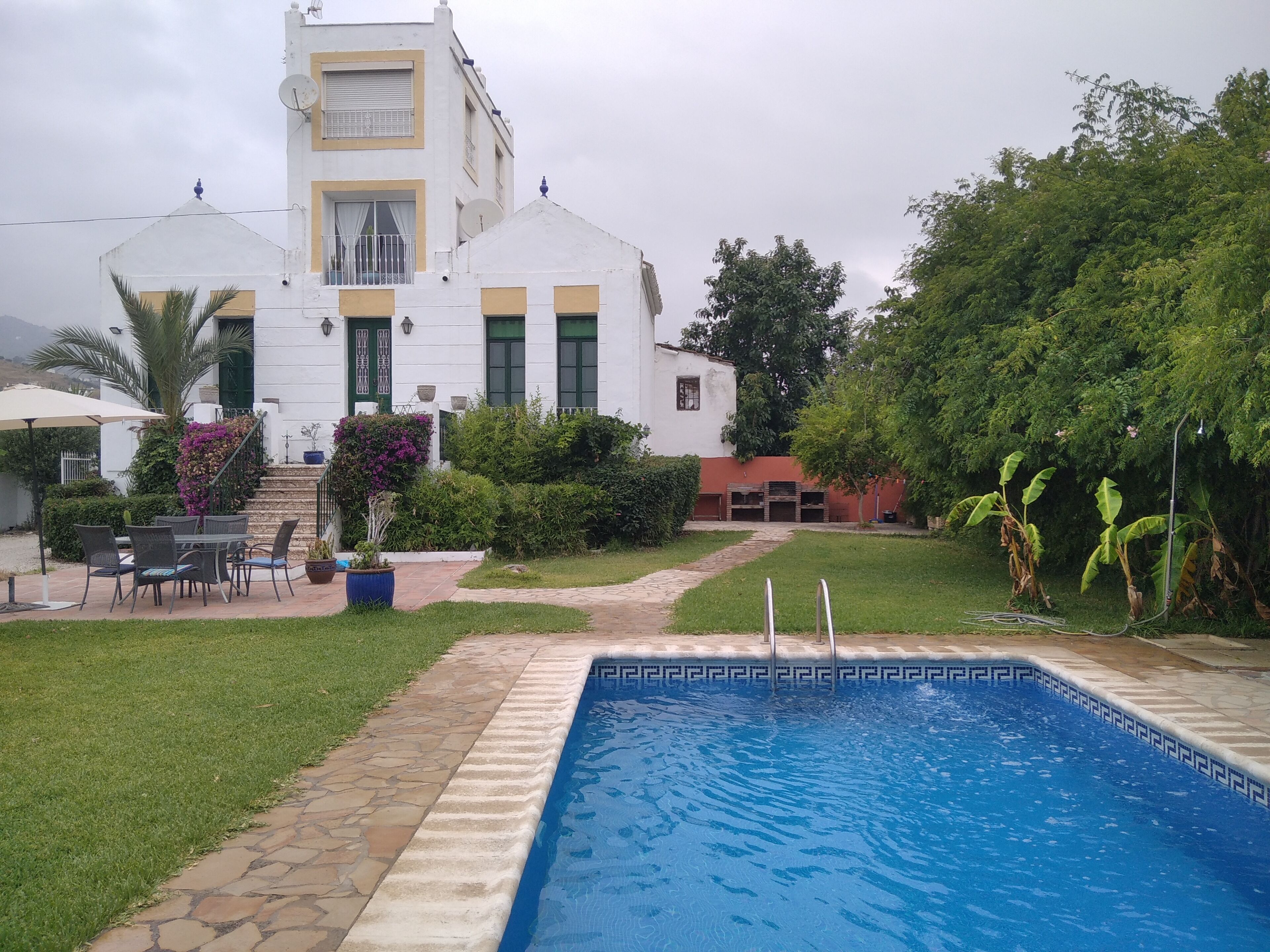 A swimming pool with a stone border, surrounded by a well-maintained lawn and a patio area with outdoor furniture.