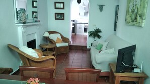 Una sala de estar con un sofá, dos sillones de mimbre, una mesa de centro, un televisor y una chimenea.