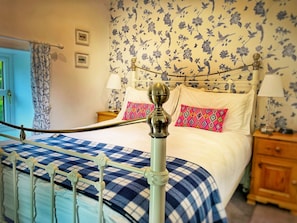 Una cama con estructura metálica, colcha a cuadros y papel tapiz con estampado floral.