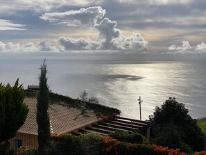 A coastal view with a clear sky, a calm sea, and a building with a tiled roof and steps leading down to the water.