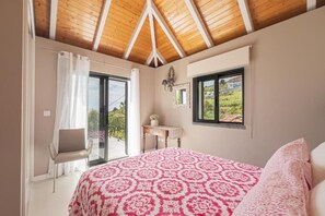 Una camera da letto con un letto grande, una sedia, una scrivania e vista su un paesaggio verde dalle finestre.