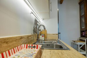A kitchen with a stainless steel sink, a wooden countertop, and a hanging rack with utensils.