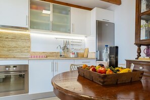 A kitchen with white cabinets, a stainless steel refrigerator, a wooden fruit bowl on the counter, and a built-in oven. - Special offer: House w / pool set in a romantic and idyllic location. (Prazeres - Calheta)
