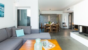 A modern living room with a gray sofa, a wooden coffee table, and a dining area with a stone wall and wooden furniture. - Villa Blanche - Top quality villa surrounded by nature, close to the beach (Chania)