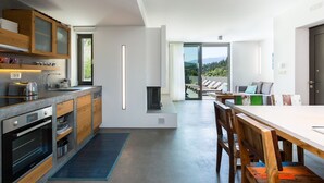 A modern kitchen with built-in appliances, a dining area with wooden chairs, and a view of a balcony with outdoor seating. - Villa Blanche - Top quality villa surrounded by nature, close to the beach (Chania)