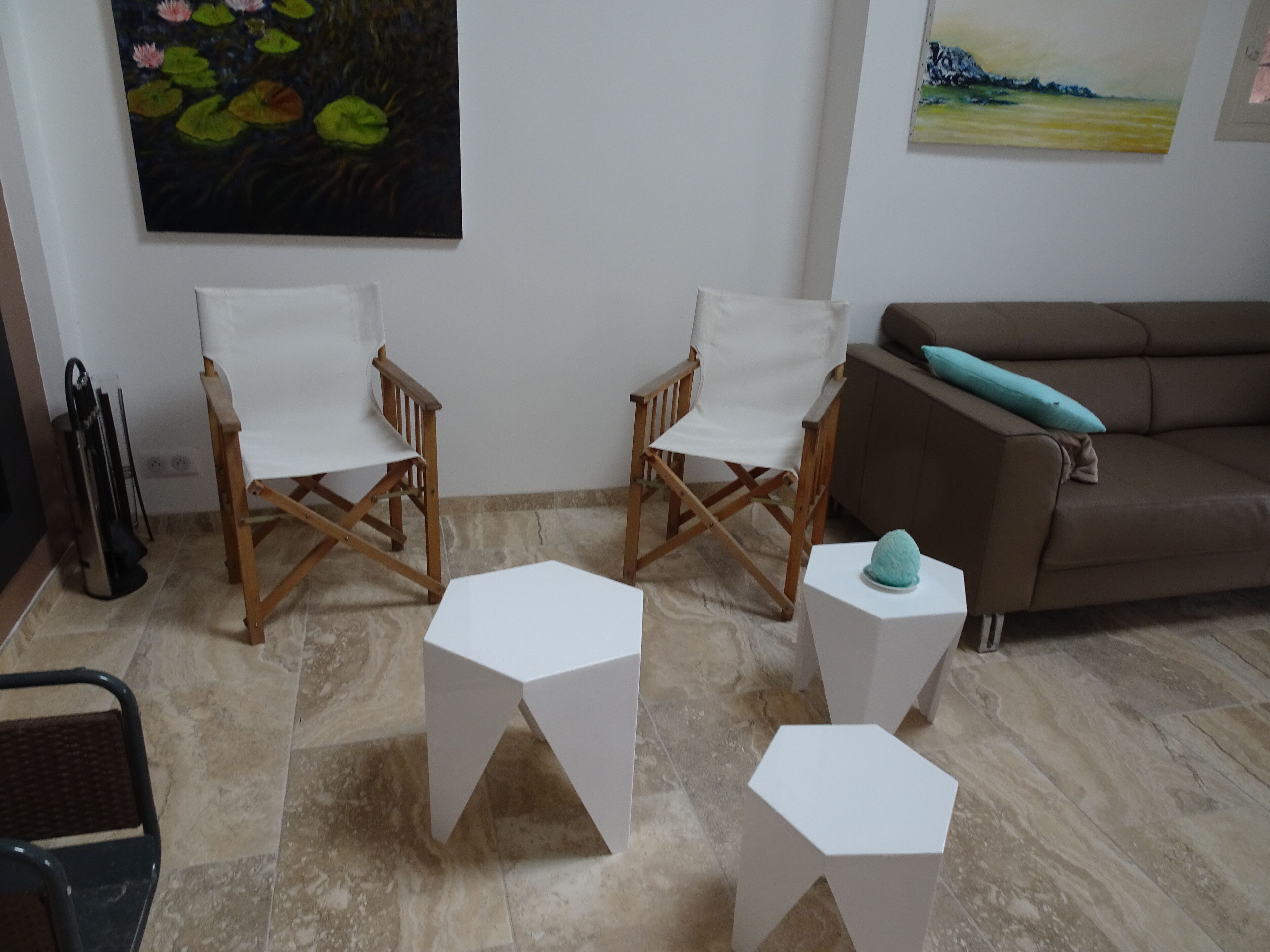 Ein Zimmer mit zwei Holzstühlen, einem weißen Tisch, einem braunen Sofa und einem Bild an der Wand.