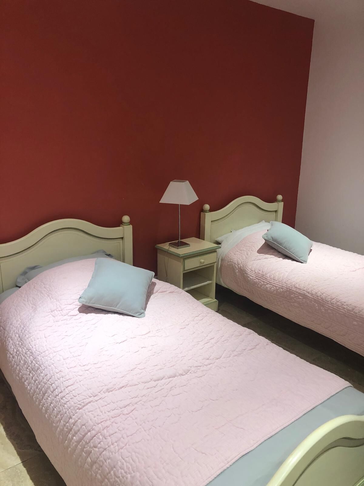 A room with two beds, each with a pillow and a nightstand with a lamp.