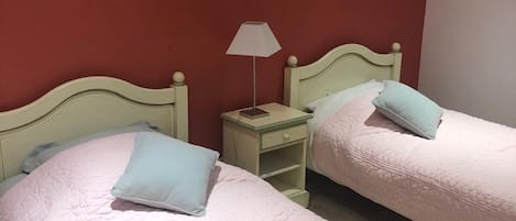 A room with two beds, each with a pillow and a nightstand with a lamp.