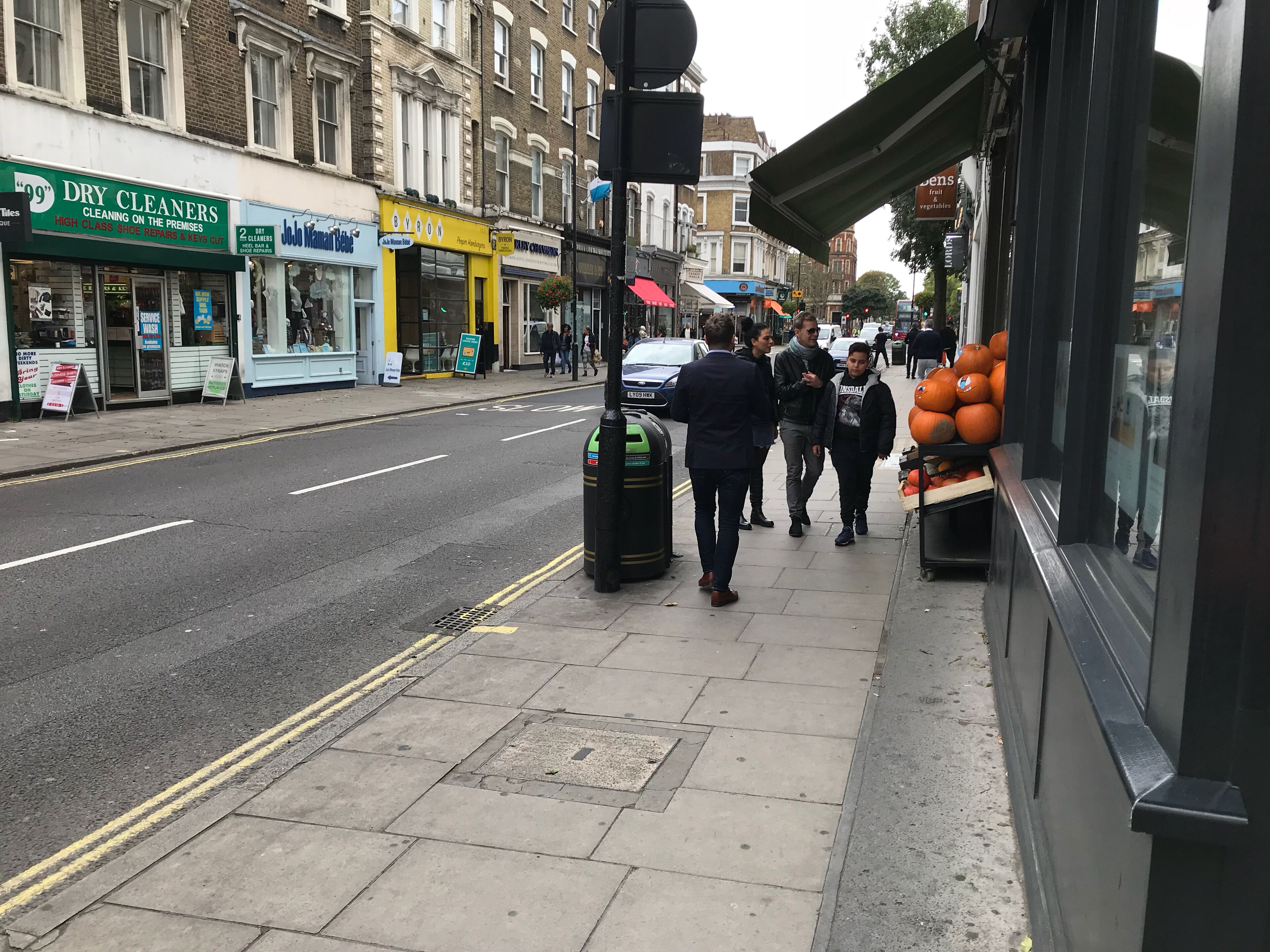 A street view with shops, including a dry cleaners and a fruit and vegetable stall.