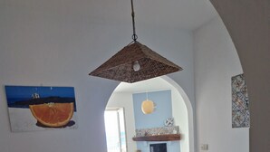 A dining area with a wooden table and blue chairs, an arched doorway leading to a living room, and a hanging light fixture.
