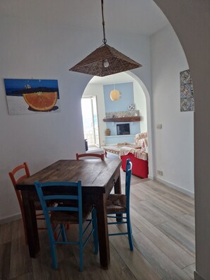 Uma área de refeições com mesa de madeira e cadeiras azuis, um arco que dá para uma sala de estar e um lustre.