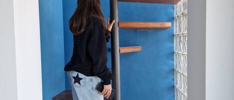 A person climbing a wooden spiral staircase in a room with blue walls and a tiled floor.