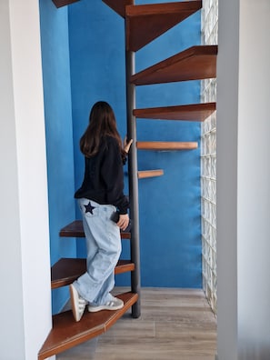 A person climbing a wooden spiral staircase in a room with blue walls and a tiled floor. - Gorgeous Attic Room by the Sea. Breathtaking view (Palermo)