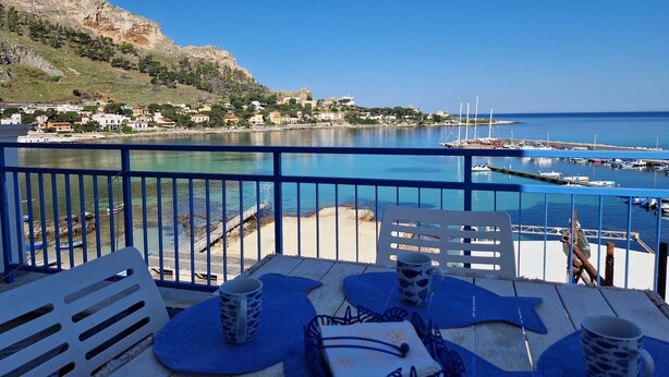 A balcony with a view of a marina, a sandy beach, and a hillside with buildings.