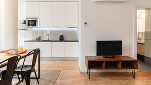 A modern kitchen with white cabinets, a microwave, and a coffee maker. There is a dining area with a wooden table and chairs, and a TV on a wooden stand. - Galerias On Trend Nightlife by Feel Porto (Oporto)