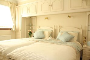 A double bed with a white headboard and two pillows, a nightstand with a lamp, and a window with curtains.