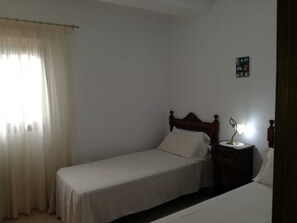 A small, simple bedroom with a single bed, a nightstand, and a lamp.