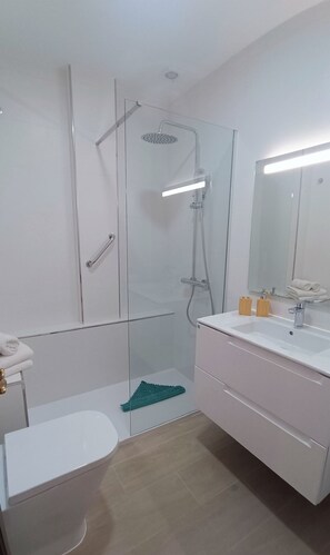 Een moderne badkamer met een douche met glazen wand, een wit wastafelmeubel en een spiegel met verlichting erboven.