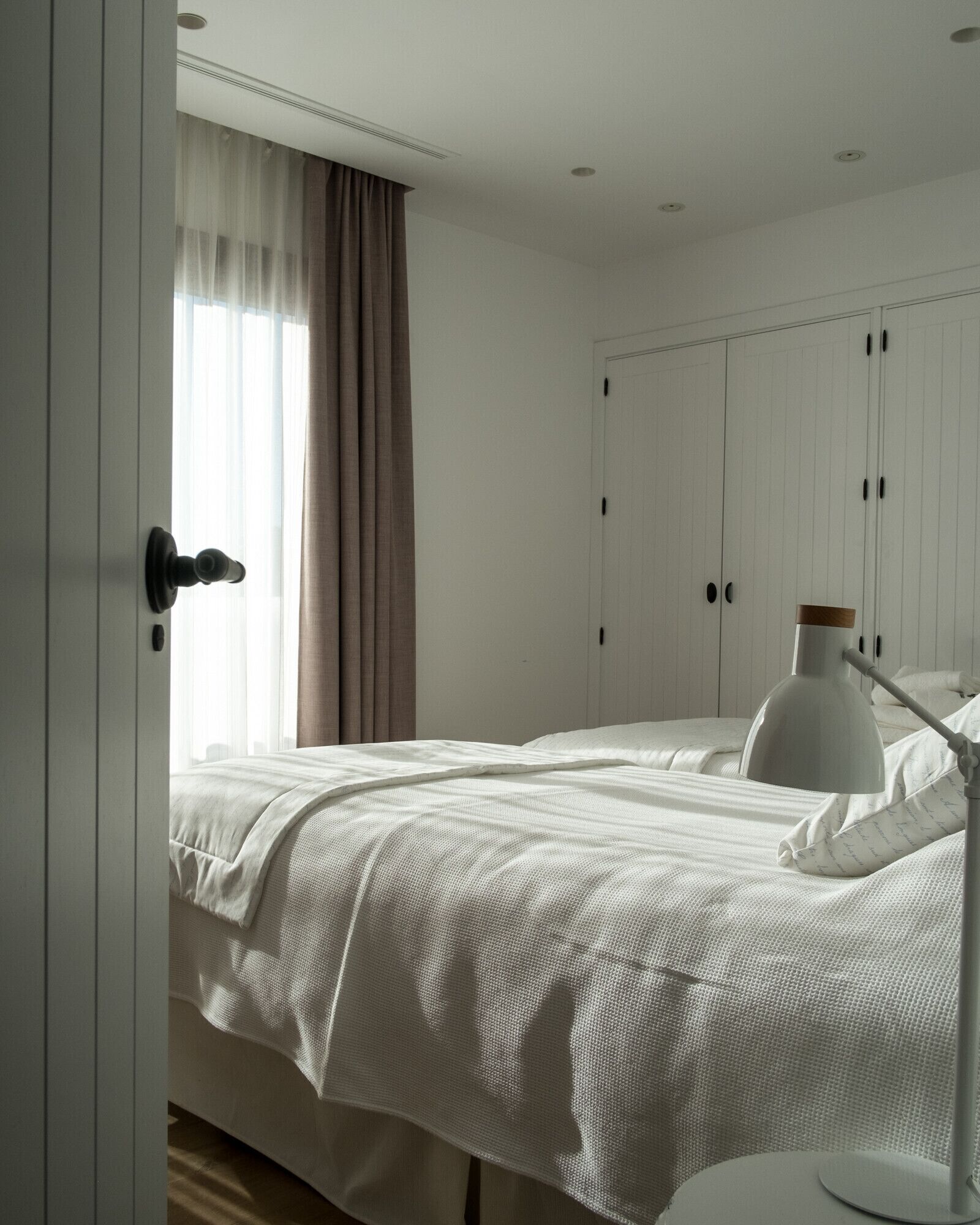 A bedroom with a bed, a bedside lamp, a wardrobe, and a window with curtains.