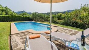 A swimming pool with a lounge area, an umbrella, and a bottle of wine on a table. - Villa Es Coste Rafal By SunVillas Mallorca (Pollença)