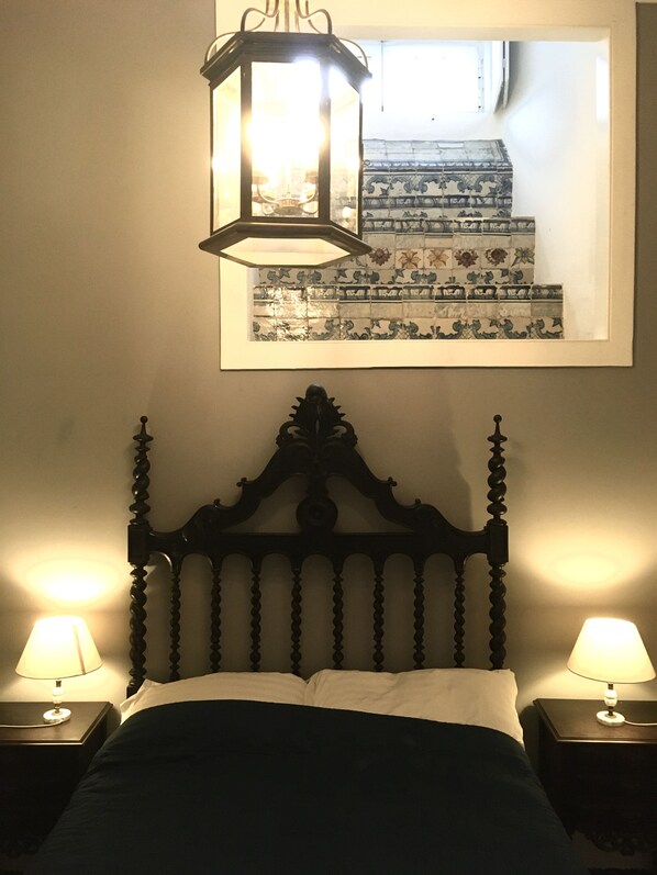 A bedroom with a bed, two bedside lamps, a wall-mounted mirror, and a decorative ceiling light fixture. - Spacious, Traditional in Historic Lisbon, with air-conditined & central heating (Lisbon)
