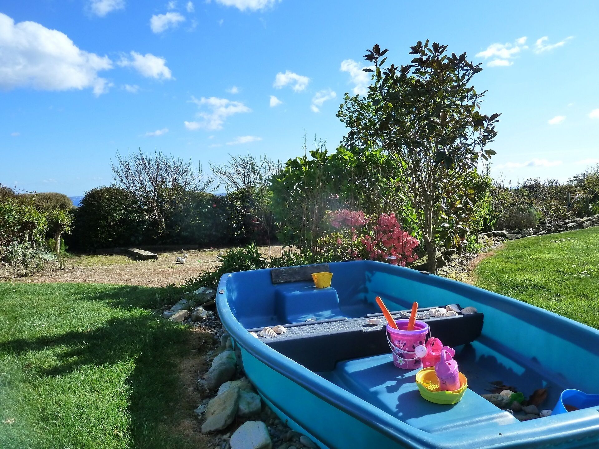 A blue boat with a paddle, a yellow bucket, and a pink cup on a grassy area.