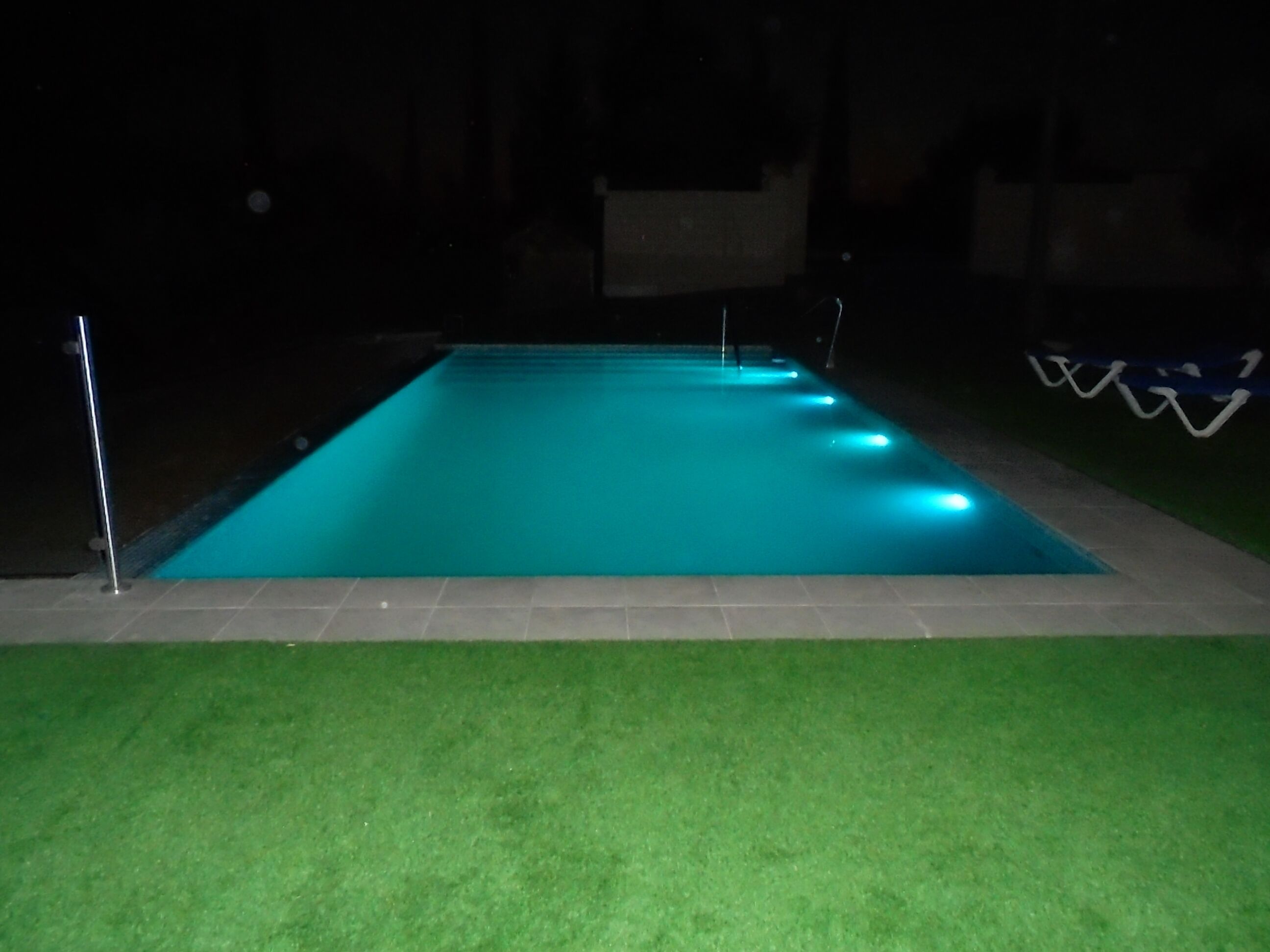 A rectangular swimming pool with a tiled edge and a surrounding grassy area.