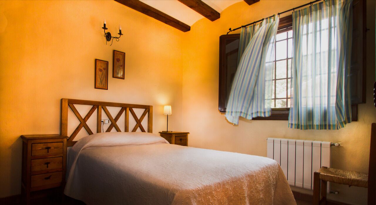Een slaapkamer met een houten hoofdbord, een bed met een witte dekbedovertrek, twee nachtkastjes, een venster met gordijnen en een radiator.