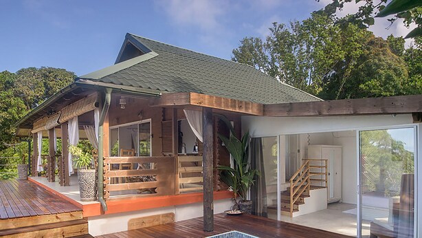 Ein modernes Haus mit Swimmingpool, einer Holzterrasse und Glastüren, die auf eine überdachte Terrasse führen.