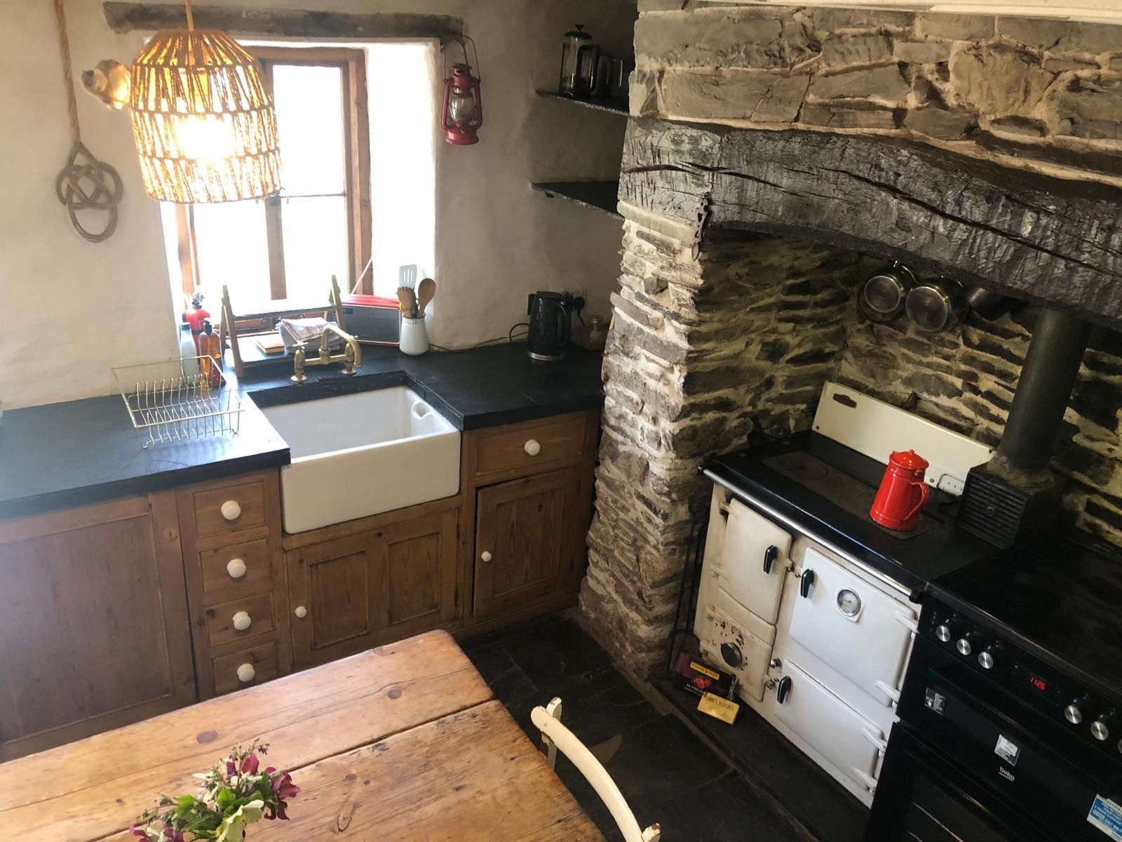 A kitchen with a stone wall, a sink, a stove, and a wooden table.