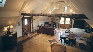 A spacious loft with a high ceiling, exposed wooden beams, a fireplace, a cozy seating area, and a dining table. - The Coach House is a retreat from the outside world. (Tenbury Wells)