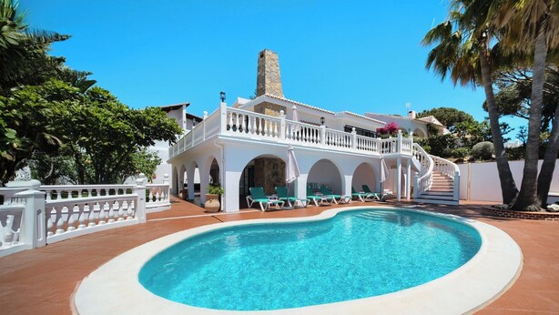 A pool area with a clear blue pool, white balustrades, and green lounge chairs.