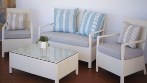 A seating area with wicker furniture, including a sofa and two armchairs, each with striped cushions. A small table with a glass top is placed in front of the sofa.