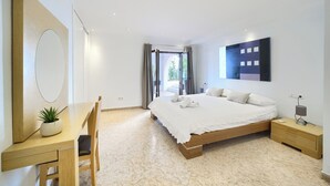 A modern bedroom with a large bed, a desk with a chair, a bedside table, and a large mirror.