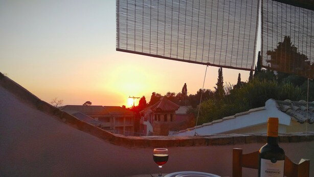 Une table dressée pour deux personnes, avec des assiettes, un verre de vin rouge et une bouteille de vin, offrant une vue sur le coucher du soleil.