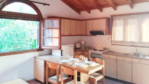 Une cuisine compacte avec des meubles en bois, une table à manger pour quatre personnes et une fenêtre donnant sur un paysage verdoyant.