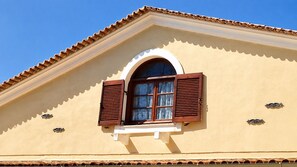 A building with a pitched roof, a window with wooden shutters, and decorative metal elements.