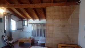 Une chambre avec deux lits simples, un plafond en bois, une petite table avec un panier, une chaise et une fenêtre avec des rideaux.