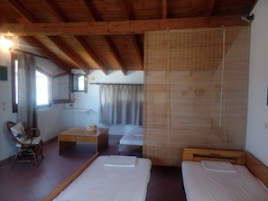 Une chambre avec deux lits simples, un plafond en bois, une petite table avec un panier, une chaise et une fenêtre avec des rideaux.